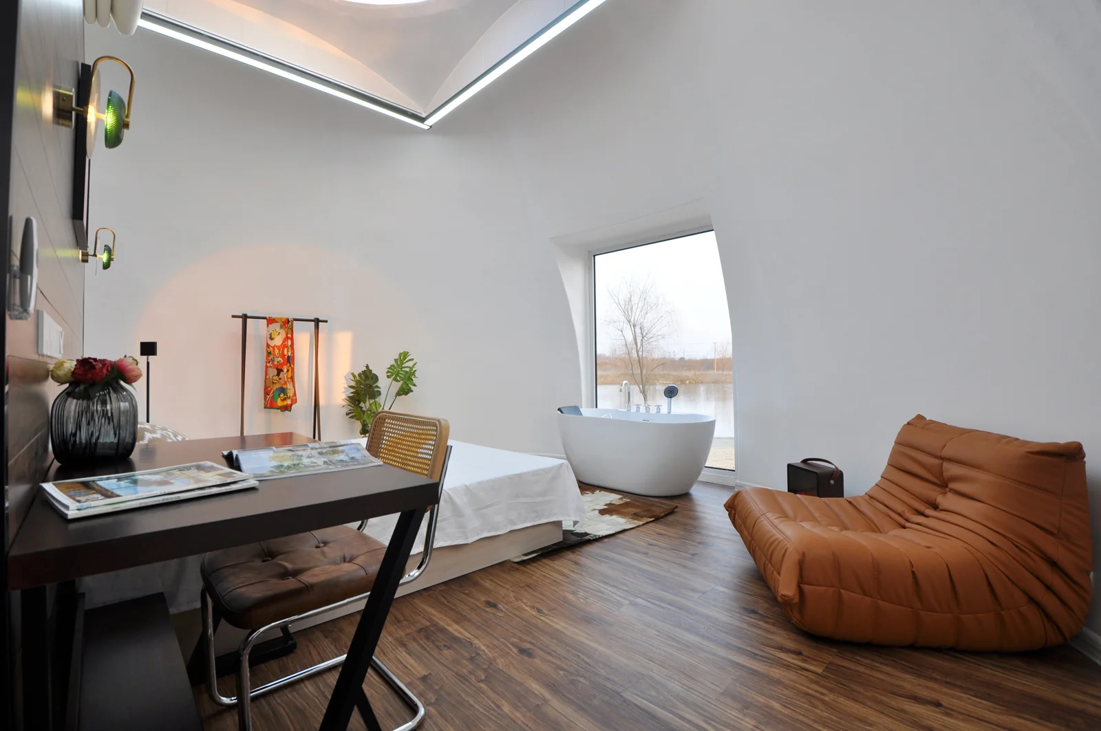 Photographed MarsDome interior with a leather lounge chair, sleeping area and a freestanding bath beside a window.