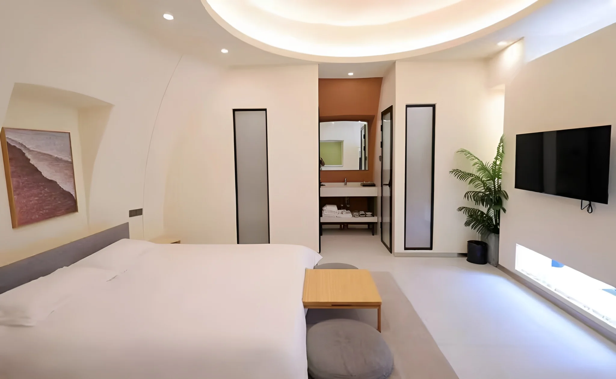 Wide room view with a bed, vanity, television and curved ceiling.