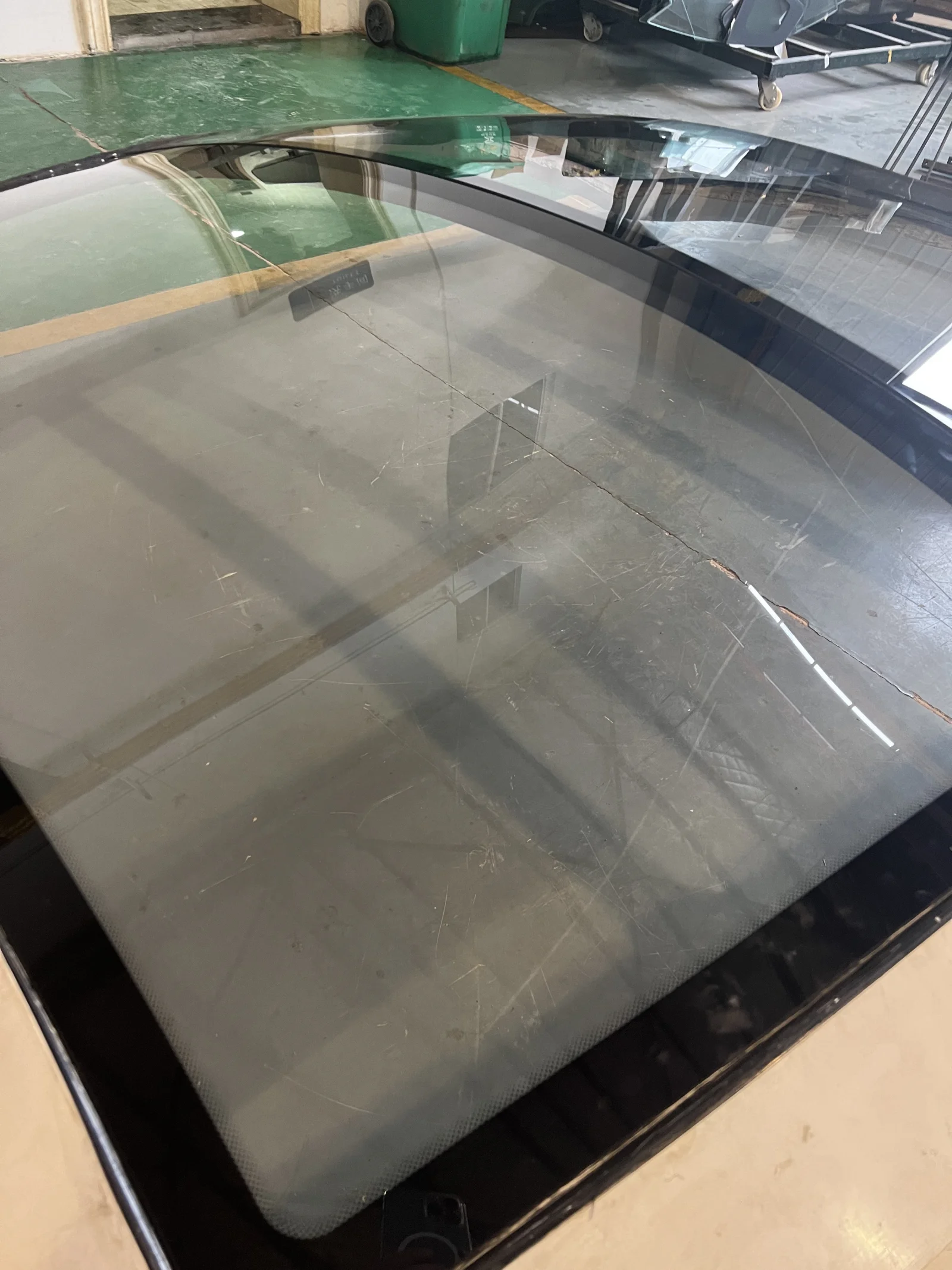 Curved double-glazed glass close-up, transparent enough to see the floor through it, with a dark ceramic frit border shielding the seal